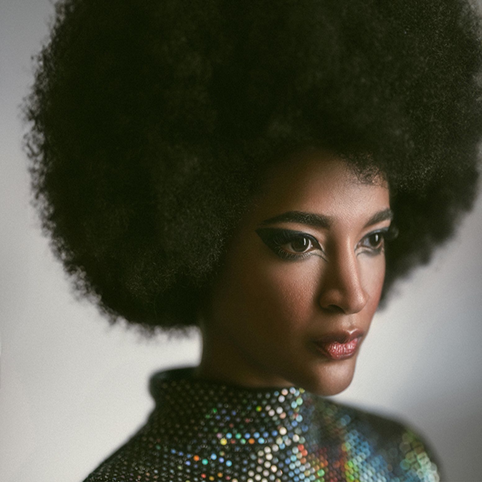 Striking beauty portrait of a woman with dramatic winged eyeliner, flawless skin, and a voluminous afro hairstyle, styled in a shimmering sequin outfit.