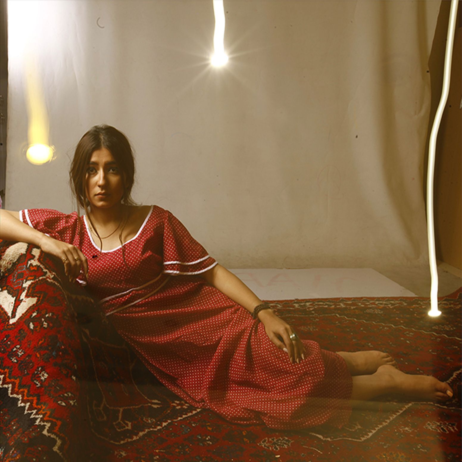 Woman reclines barefoot on a richly patterned Persian rug in a red dress, under warm ambient light trails, evoking cultural symbolism and introspective fine art photography.